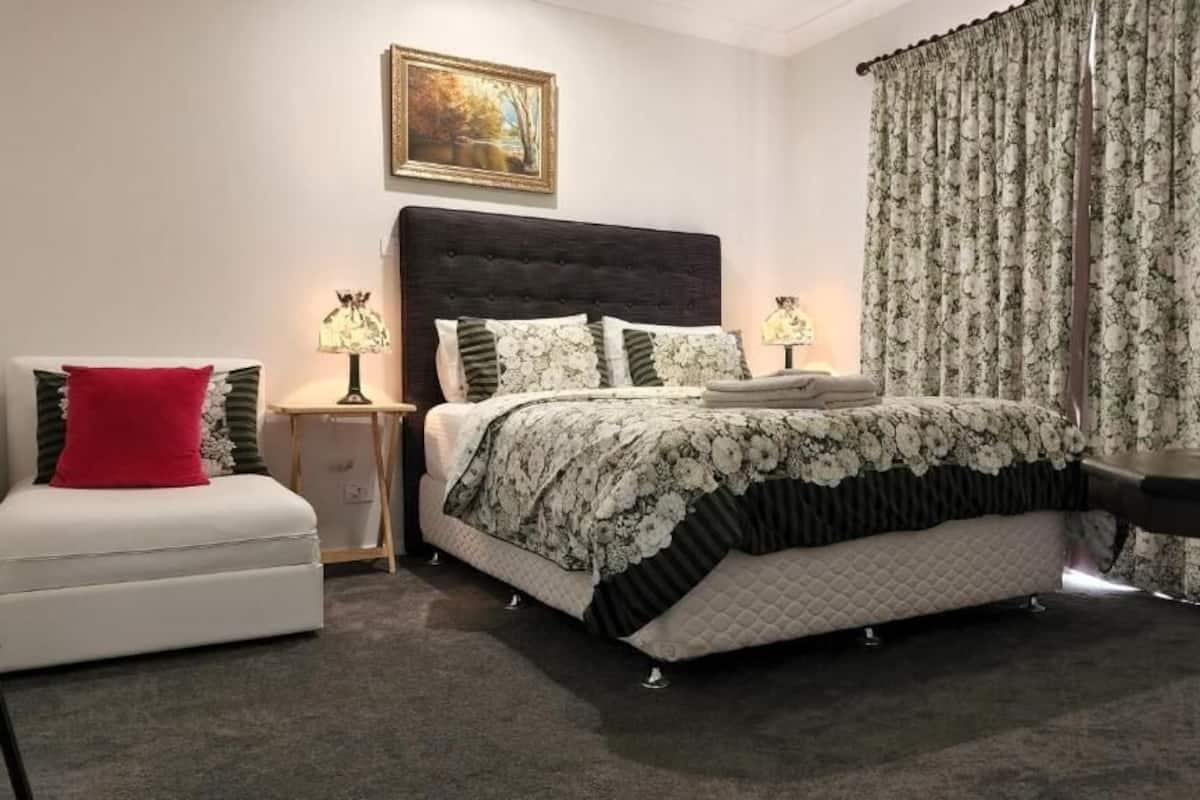 Ein ordentlich eingerichtetes Schlafzimmer mit einem großen Bett, einem Nachttisch mit Lampen, einem Sessel und einem Schreibtisch.
