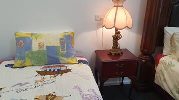 A bedroom with a bed featuring a colorful quilt with animal illustrations, a bedside lamp, a wooden nightstand, and a mirror.