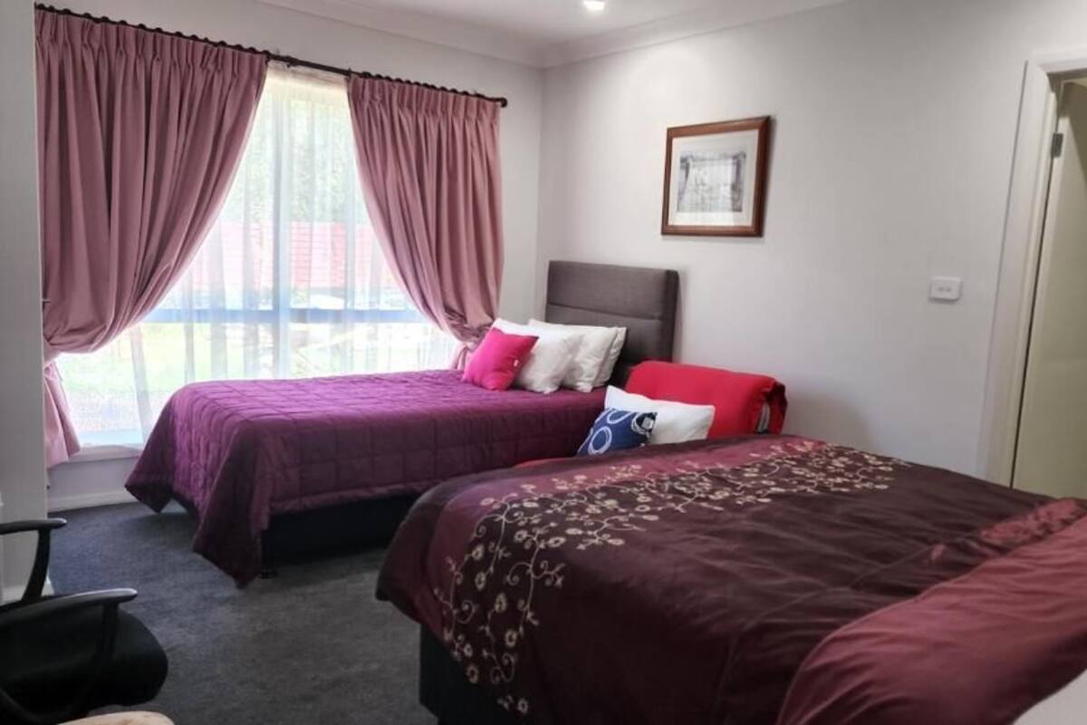 Ein Hotelzimmer mit zwei Betten, einem Kopfteil, einem gerahmten Bild an der Wand und Blick durch große Fenster nach draußen.