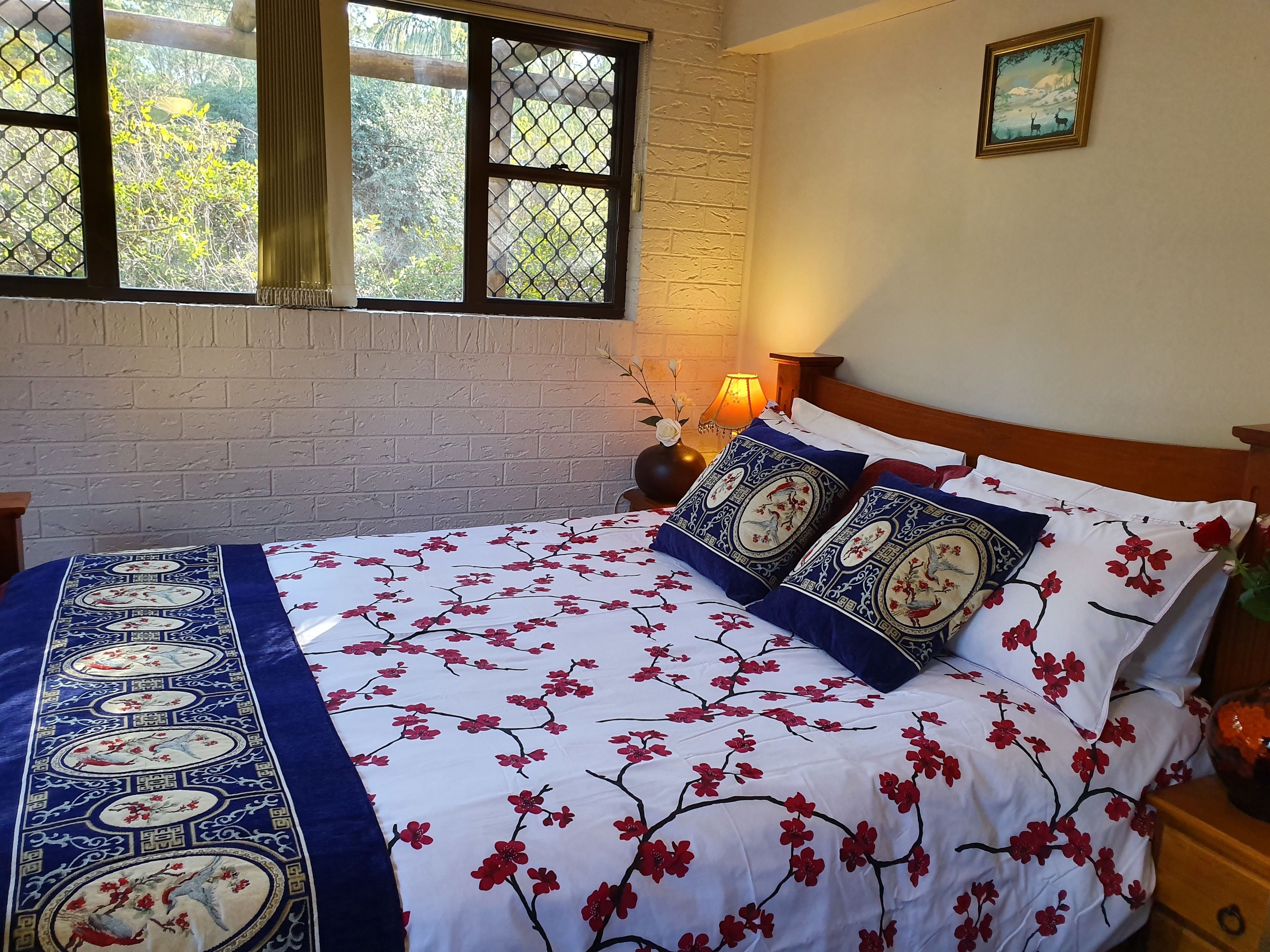 Un dormitorio con cama, mesita de noche, lámpara y ventana con vista a árboles.