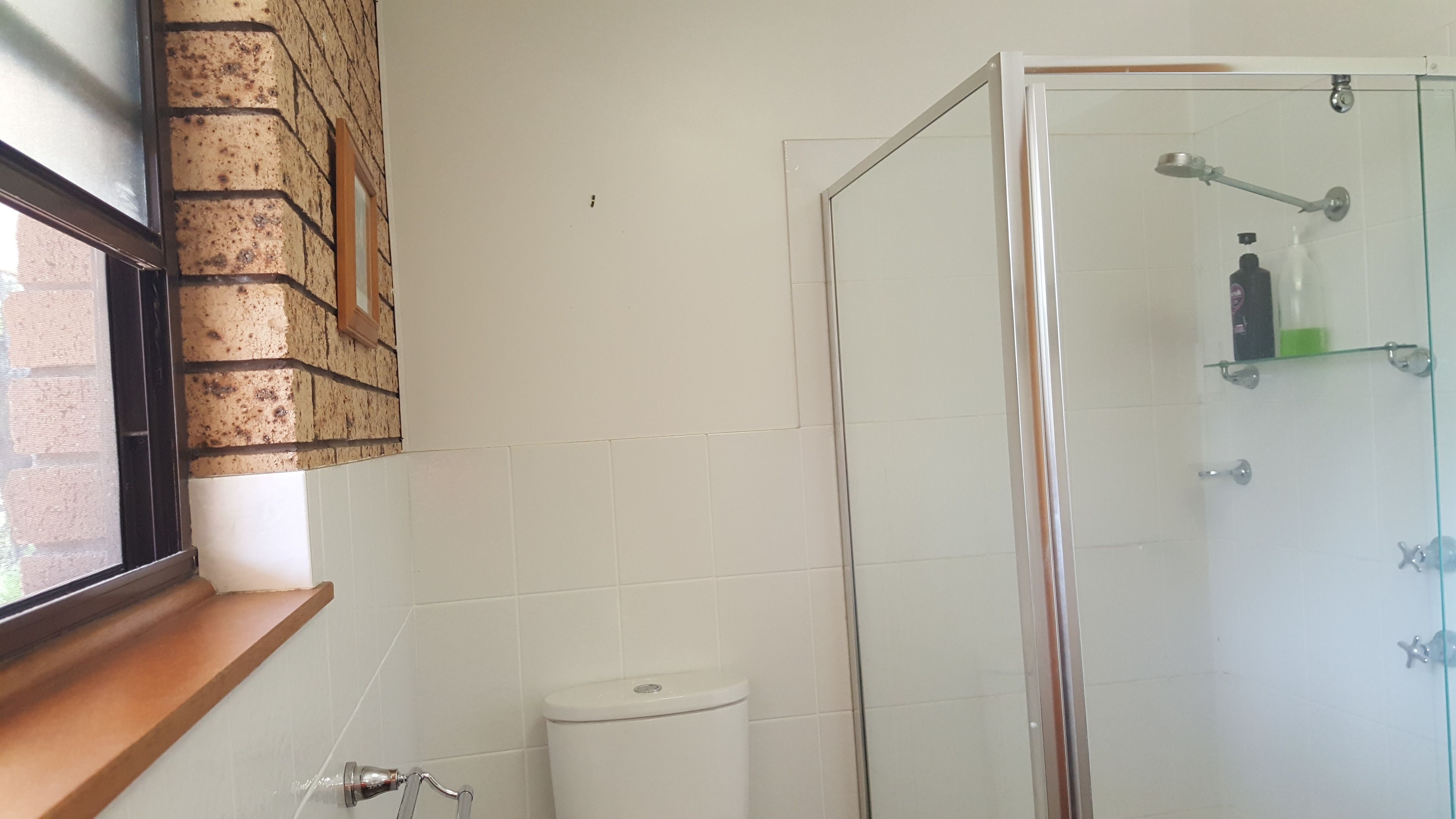 Ein Badezimmer mit Duschkabine aus Glas, Toilette und Fenster zur Ziegelwand.