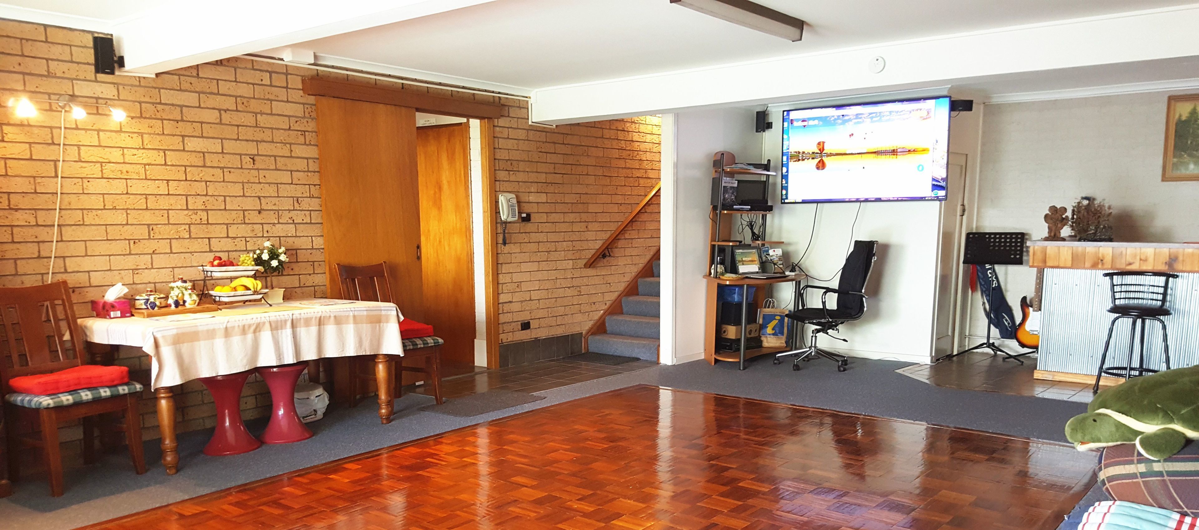 Una habitación con piso de madera, una mesa de comedor con sillas, una escalera, un escritorio con computadora y un ventanal con vistas.
