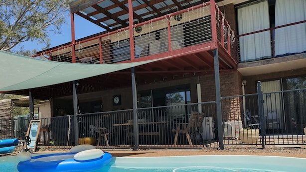 A pool area with a blue inflatable ring, a covered seating area with a table and chairs, and a building with a balcony and windows. - Gowrie Agapanthous - Hostel (Gowrie)