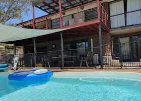 Zona de piscina con un flotador azul inflable, un área de estar cubierta con mesa y sillas, y un edificio con balcón y ventanas.