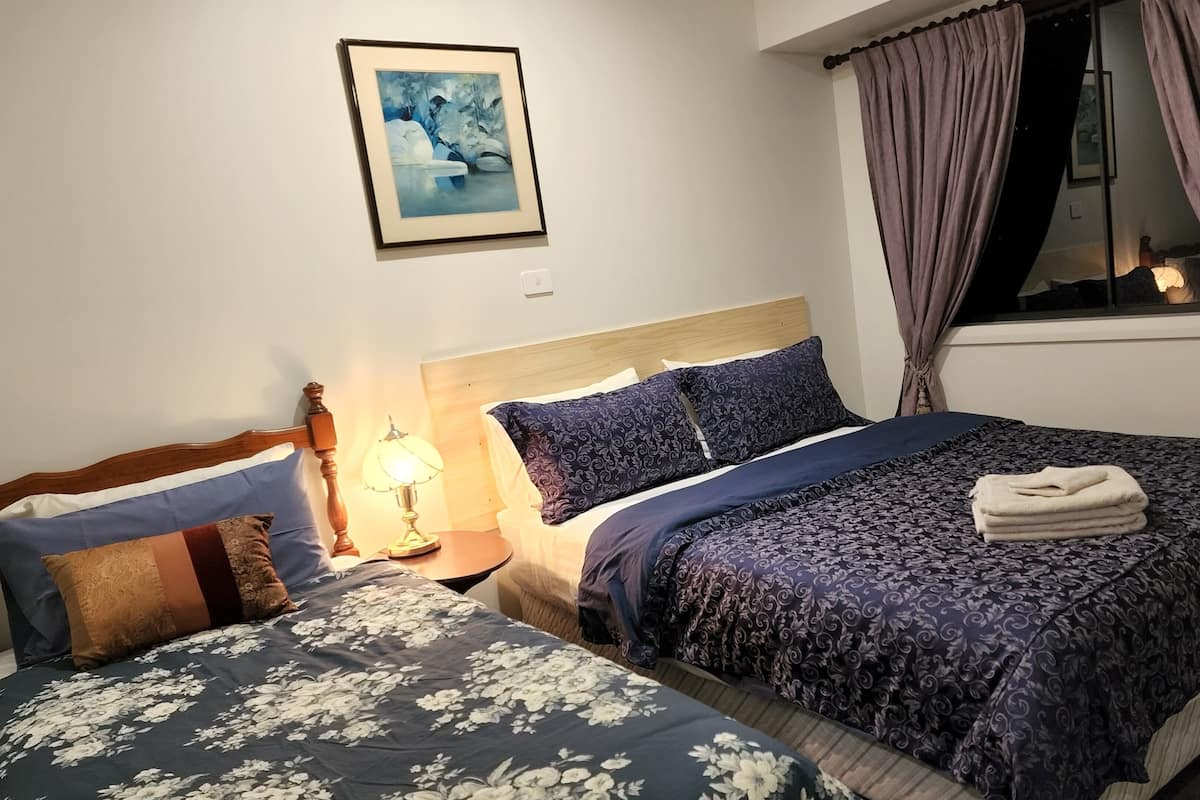 Ein Hotelzimmer mit zwei Betten, einem Nachttisch mit Lampe, einem gerahmten Bild an der Wand und einem Fenster mit Vorhängen.