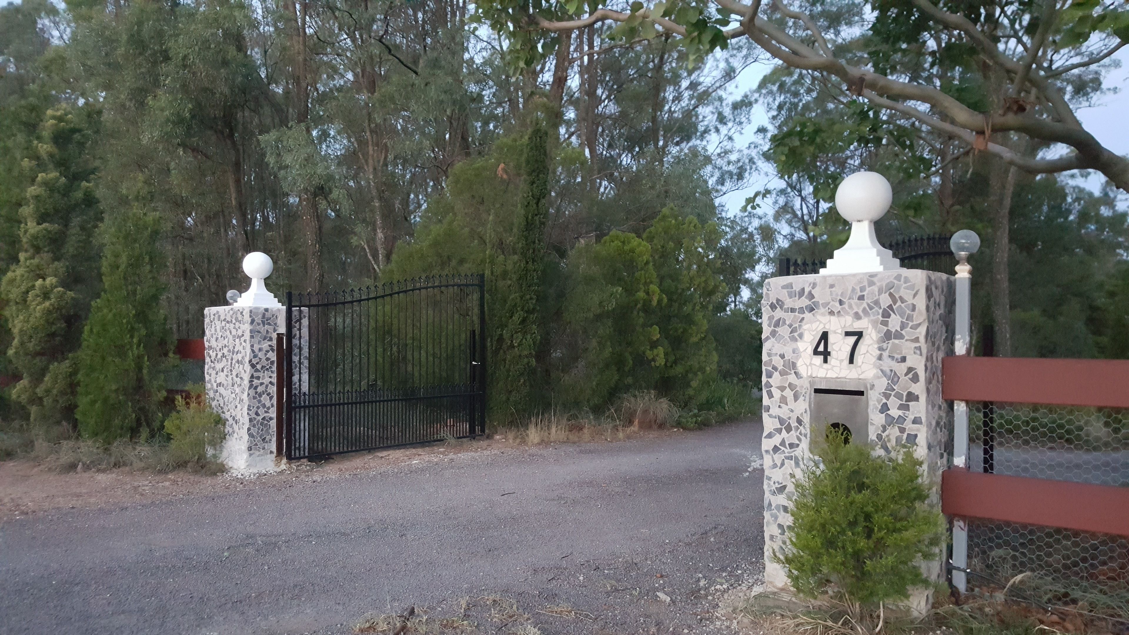 A gated entrance with a number 47 sign, surrounded by trees and a gravel path.