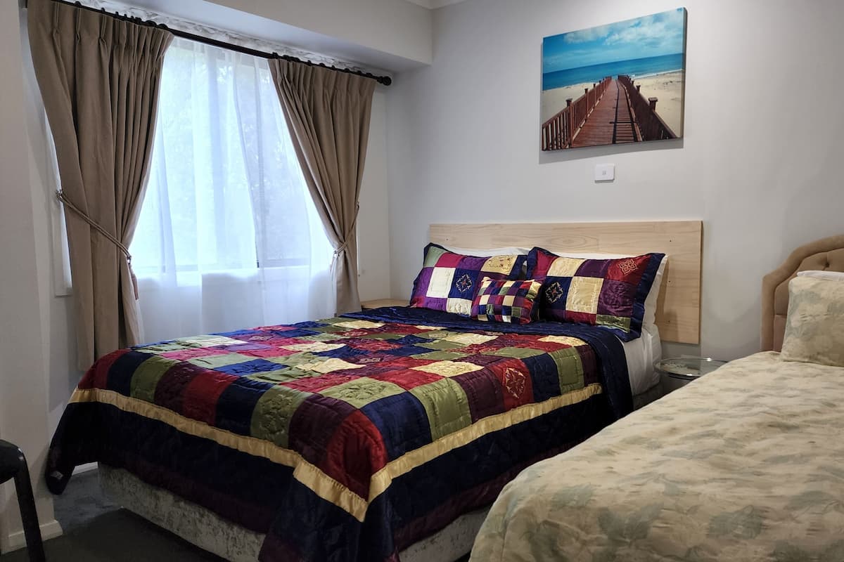 Ein Schlafzimmer mit zwei Betten, einem farbenfrohen Quilz, einem Holz-Kopfteil und einem Strandbild an der Wand.