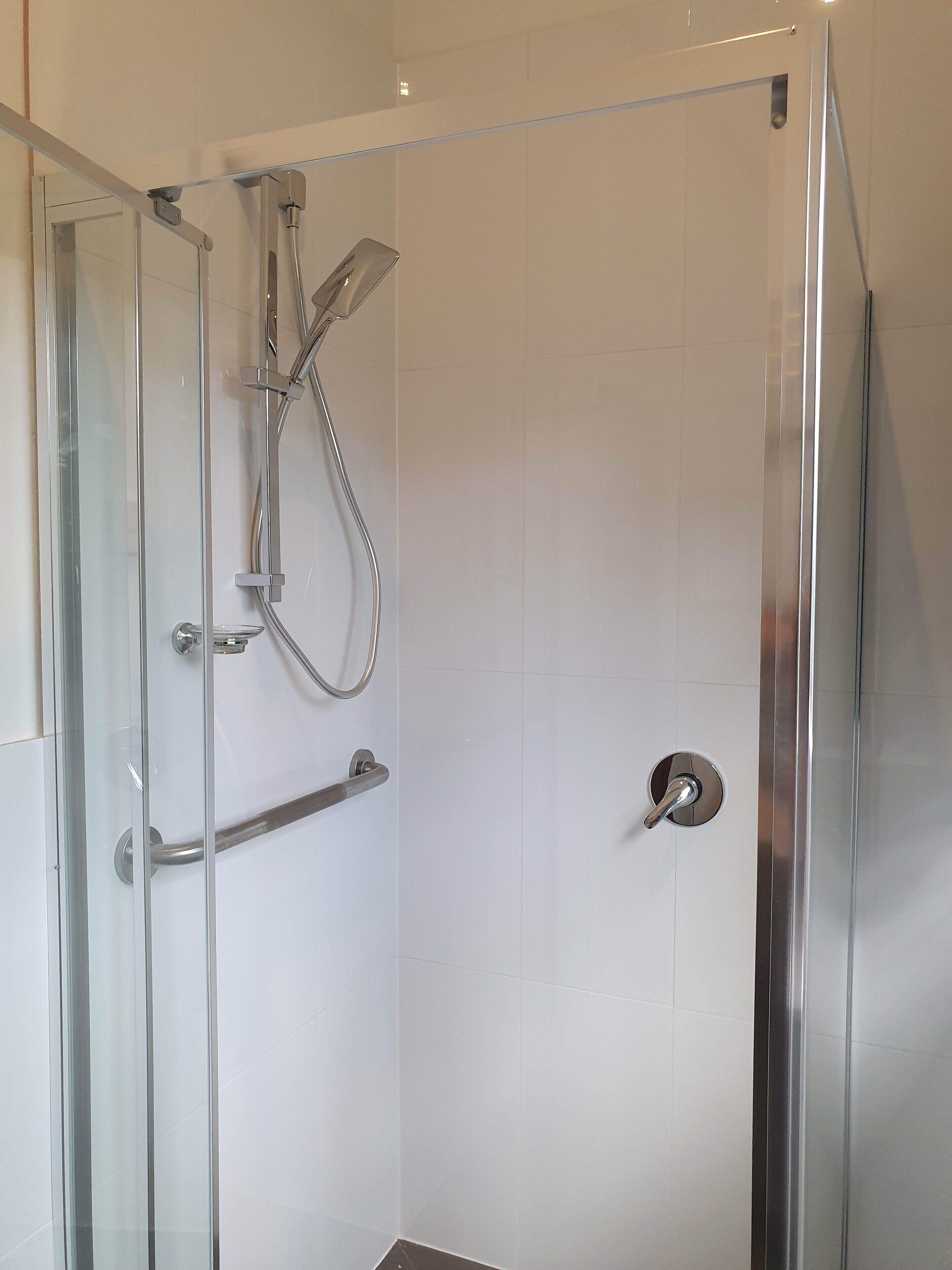 A glass-enclosed shower with a handheld showerhead and a wall-mounted faucet.