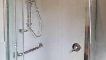 A glass-enclosed shower with a handheld showerhead and a wall-mounted faucet.