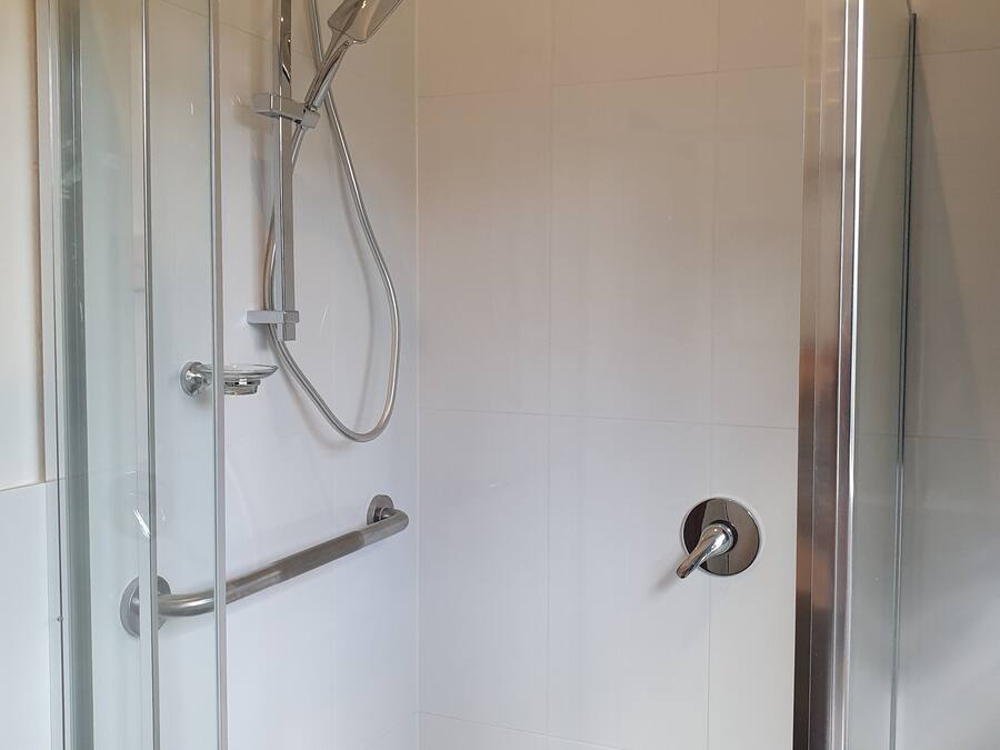 A glass-enclosed shower with a handheld showerhead and a wall-mounted faucet.