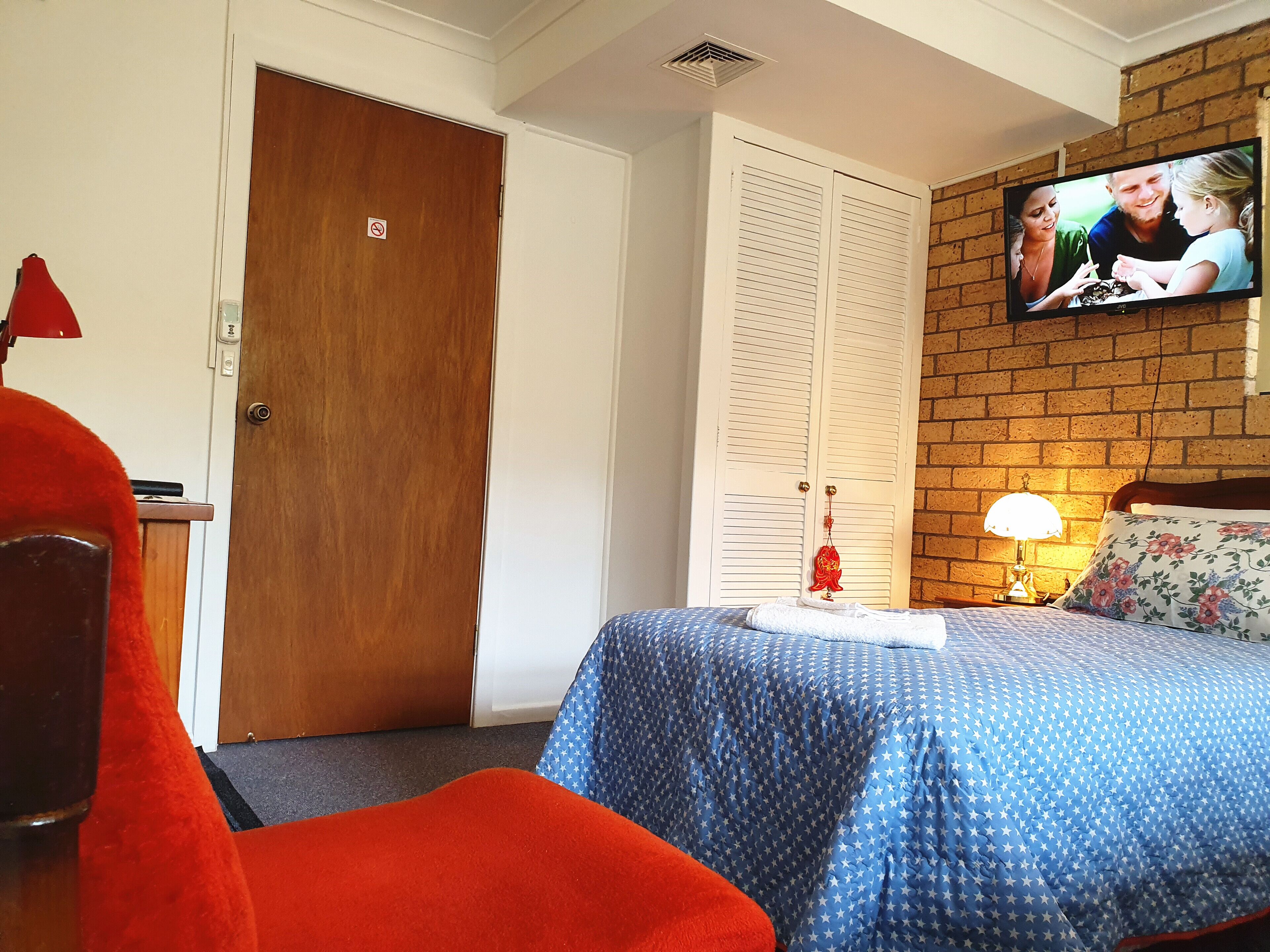 Habitación de hotel con una cama, televisor montado en la pared, una puerta de madera y una pared de ladrillo.