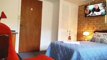 Habitación de hotel con una cama, televisor montado en la pared, una puerta de madera y una pared de ladrillo.