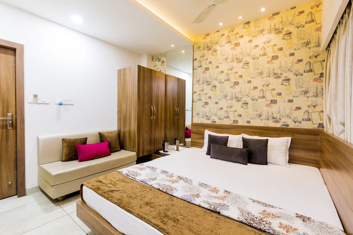 A hotel room with a large bed, a sofa, a wardrobe, and a mirror.