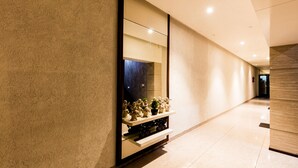 Un passadís amb un mur reflectant, una estant amb objectes decoratius i un sòl polit.