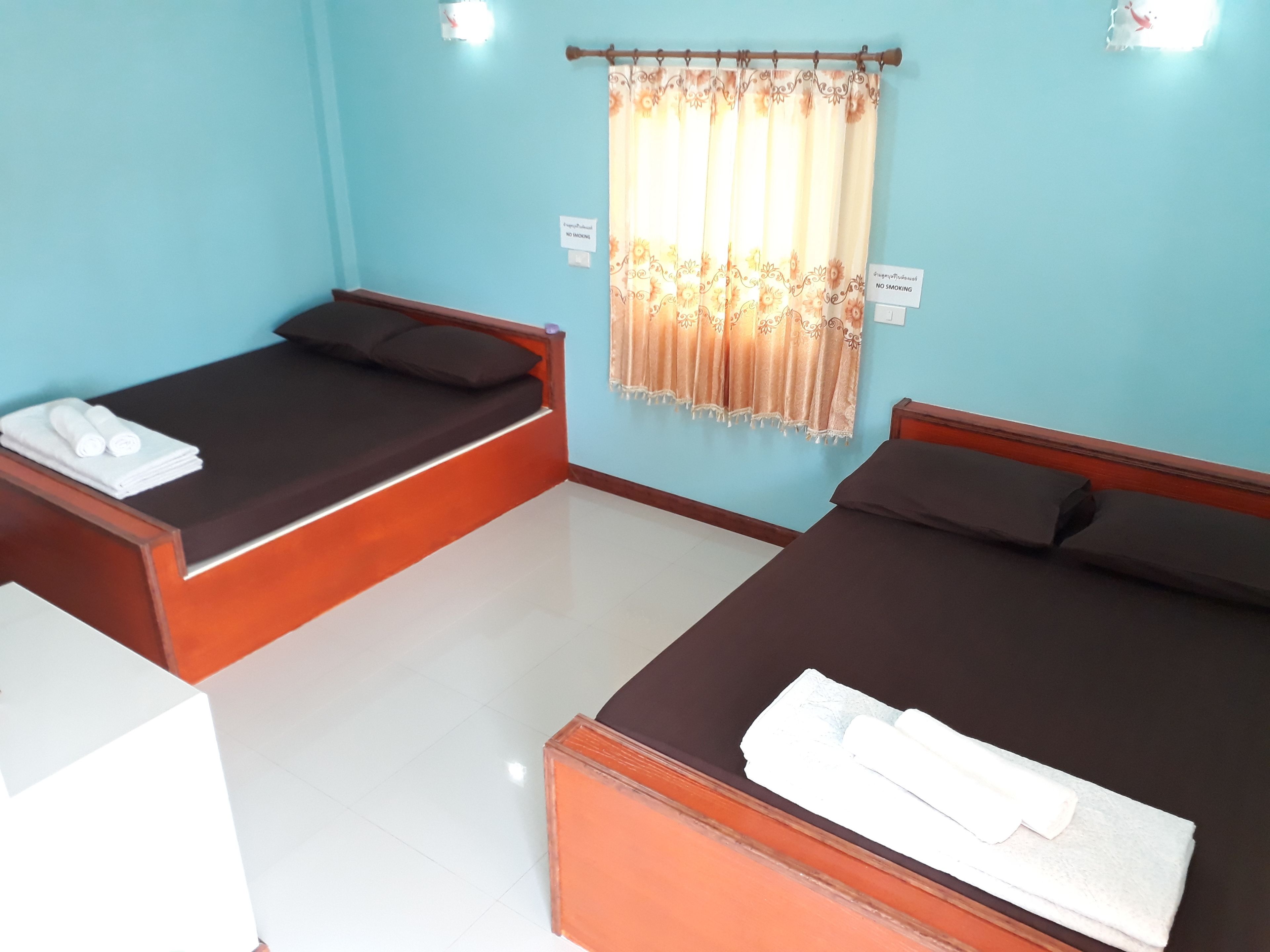 A hotel room with two single beds, a small table with towels, and a window with a curtain.