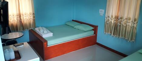 A room with a bed, a small table, and a chair. There is a sign on the wall and a window with curtains.