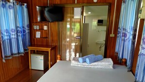 Habitación de hotel con cama, televisor, refrigerador pequeño, escritorio de madera y zona de ducha.