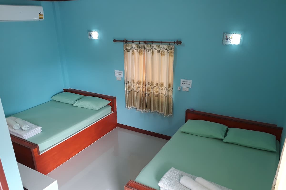 Hotellihuone, jossa on kaksi erillistä sänkyä, molemmissa vihreä patja ja tyynyt, sekä pieni pöytä, jonka päällä on pyyhe.