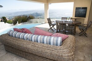 A wicker sofa with striped cushions, a dining table with chairs, and a view of a cityscape and mountains. - 32 Commodore (Knysna)