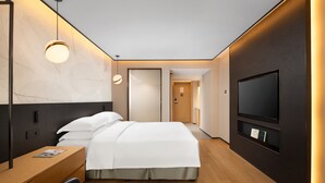 Ein modernes Hotelzimmer mit Bett, Nachttisch, Fernseher und einer kleinen Sitzecke.
