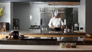 Ein Koch in einer modernen Küche mit Edelstahlgeräten, Marmorarbeitsplatten und einer aufgeräumten Anordnung.