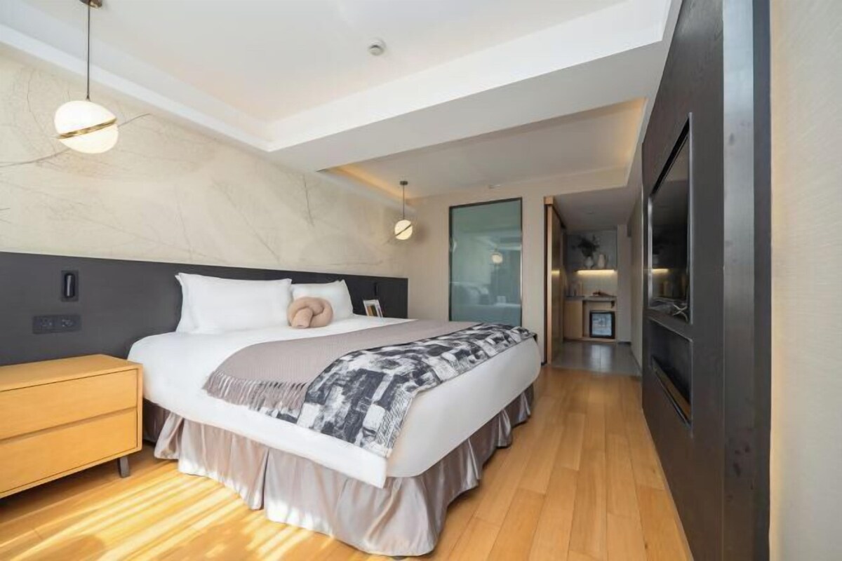 Ein modernes Hotelzimmer mit einem großen Bett, Nachttischen, einem eingebauten Fernseher und einem begehbaren Kleiderschrank.