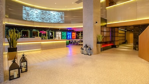 Eine moderne Lobby mit Empfangstresen, Sitzgelegenheit und einem großen Bildschirm, der eine Naturlandschaft zeigt.