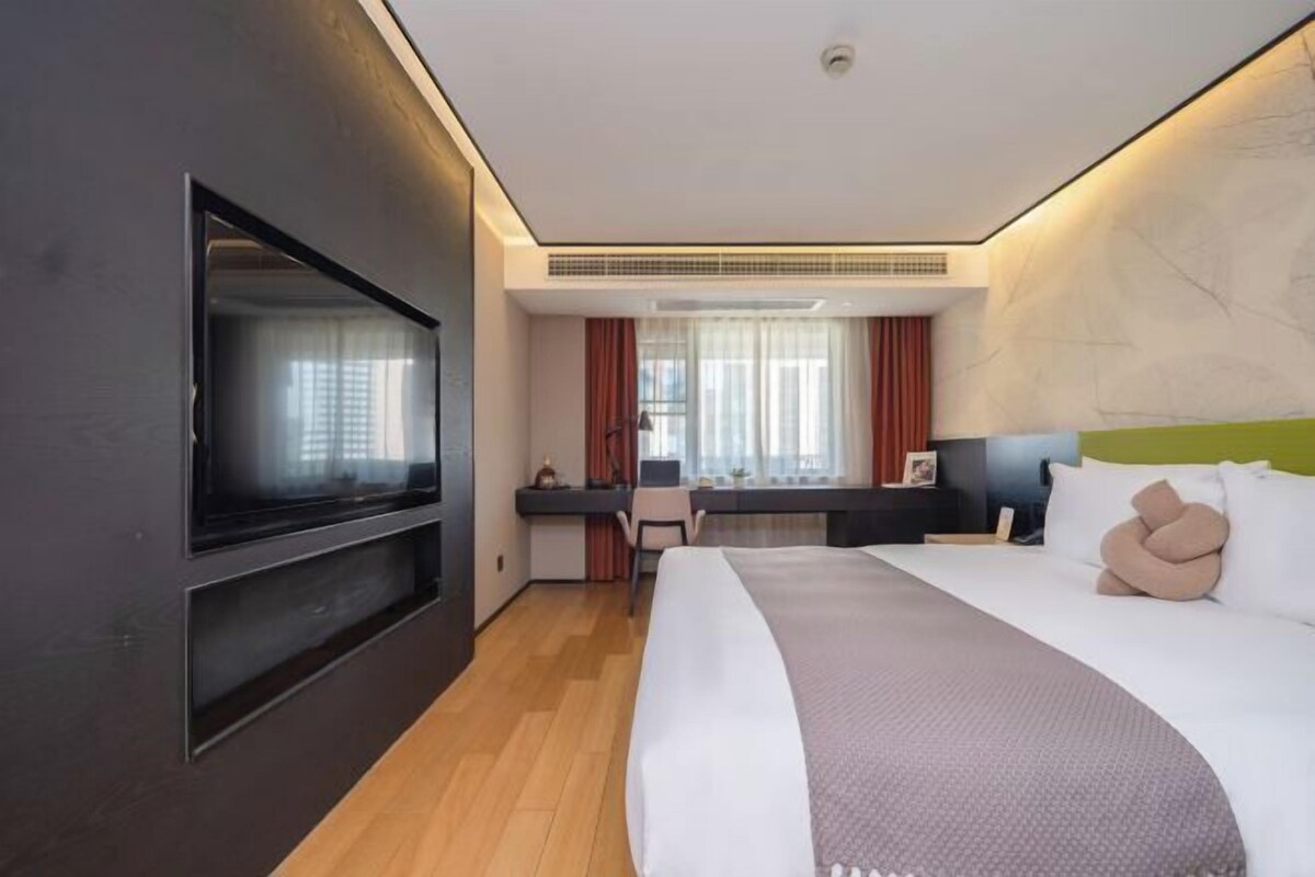 Une chambre d’hôtel comprenant un lit, un téléviseur fixé au mur, un bureau avec une chaise et une fenêtre avec des rideaux.