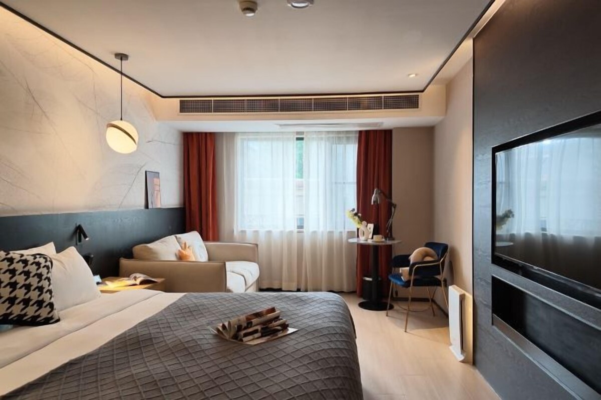 Une chambre d’hôtel moderne, dotée d’un grand lit, d’un bureau, d’une chaise, d’une télévision et d’une fenêtre avec des rideaux.