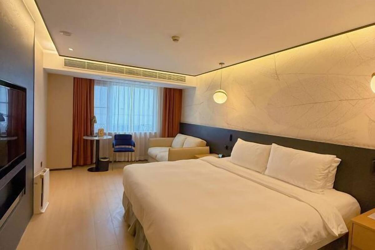 A hotel room with a large bed, a small desk, a chair, and a TV.