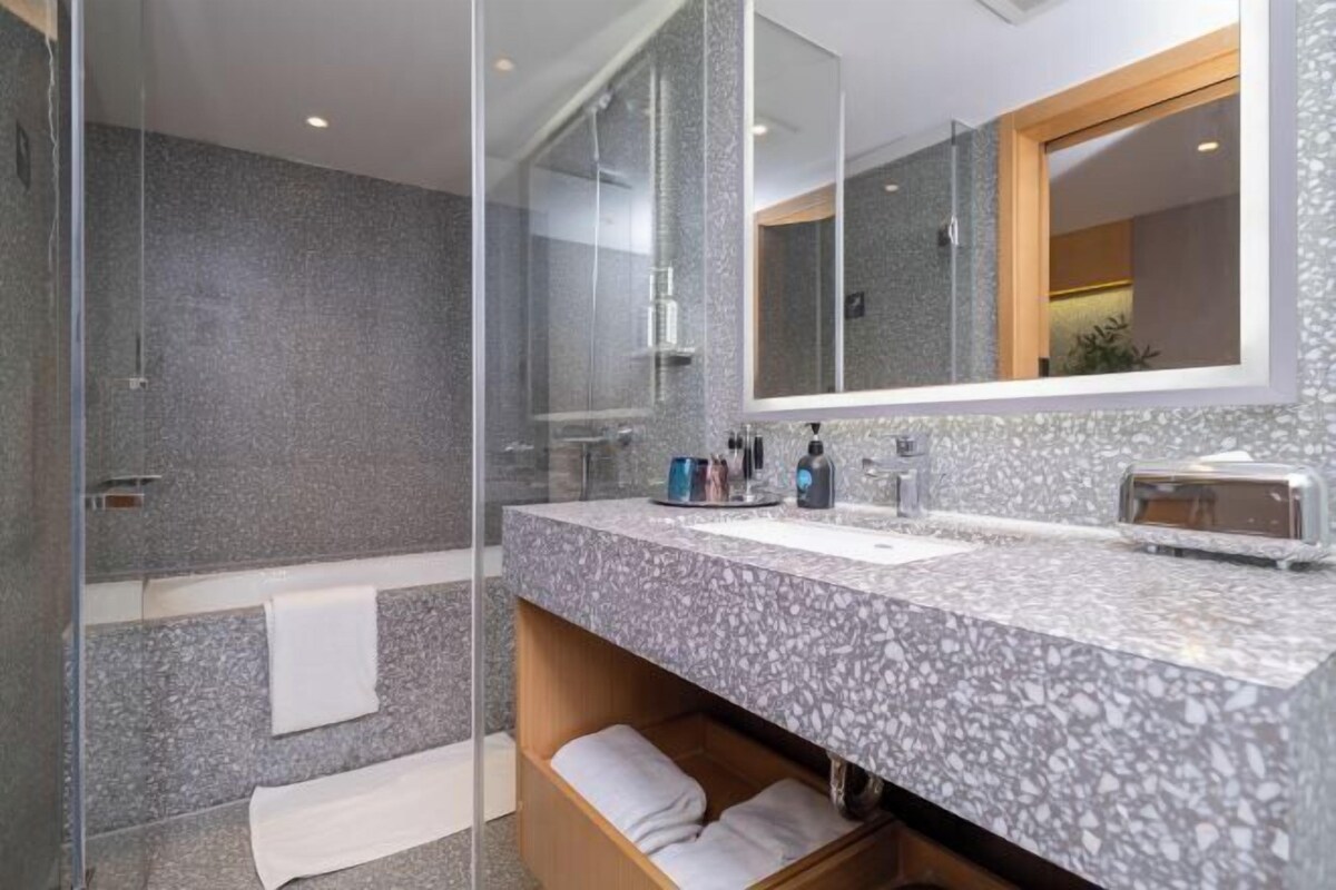 Une salle de bain moderne dotée d’une cabine de douche en verre, d’un comptoir en granit et d’un grand miroir.