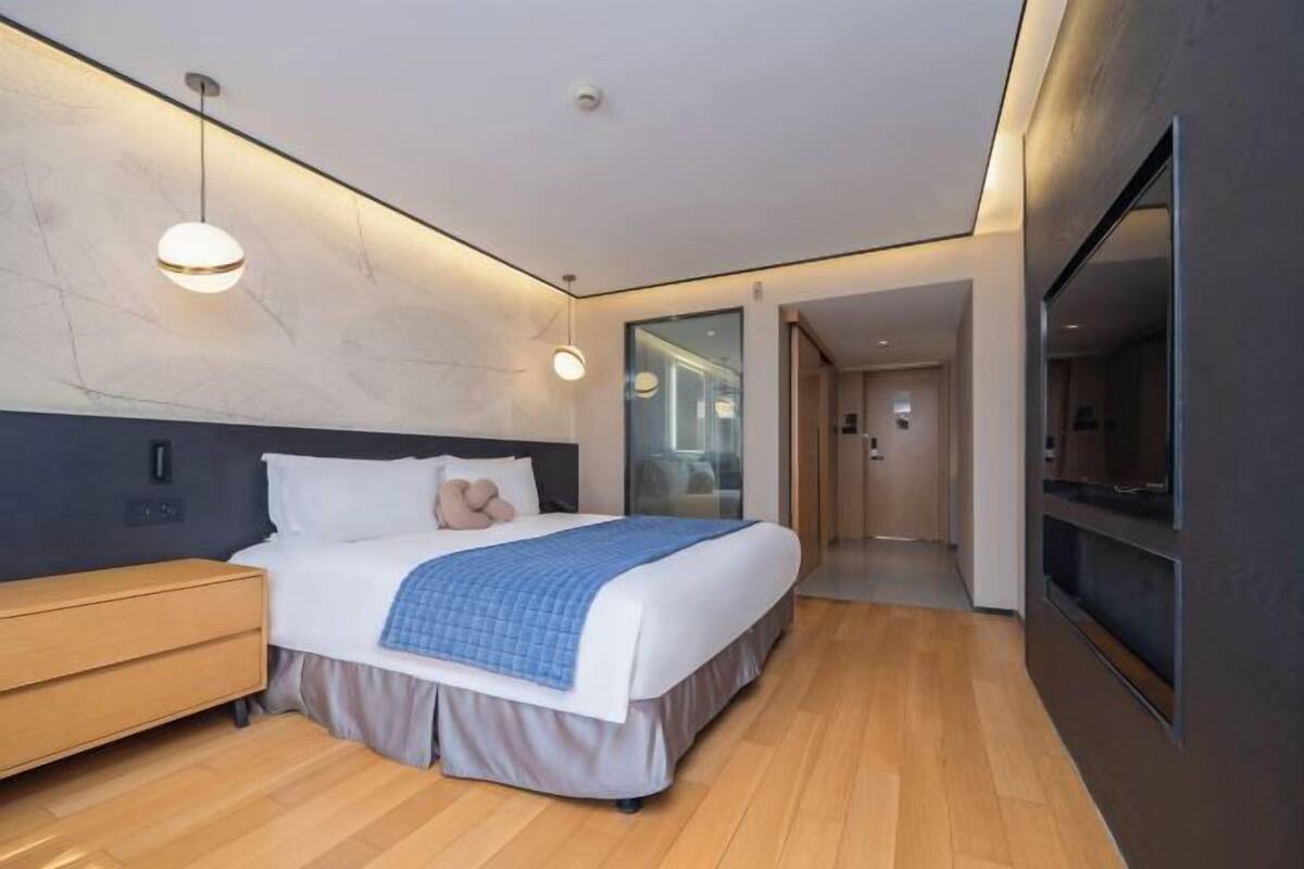 A modern hotel room with a large bed, bedside table, and a flat-screen TV.