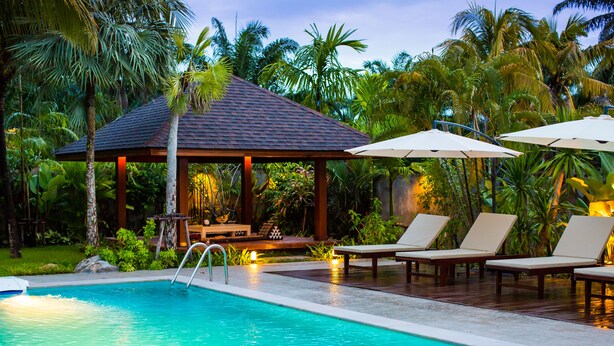 A swimming pool with lounge chairs and umbrellas, surrounded by palm trees and a gazebo. - Villa Pimmada (Krabi)