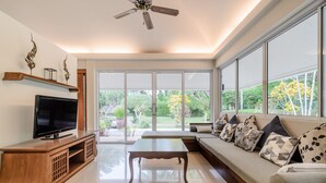 A modern living room with a flat-screen TV, wooden entertainment unit, a coffee table, and a sofa with patterned cushions. - Villa Pimmada (Krabi)