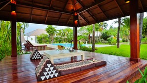 A covered outdoor seating area with a wooden deck, a table, and a sofa. - Villa Pimmada (Krabi)