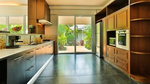 A modern kitchen with wooden cabinets, a built-in oven, and a large window overlooking a garden. - Villa Pimmada (Krabi)