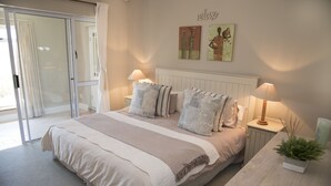 A bedroom with a large bed, two bedside lamps, a nightstand with a plant, and a sliding glass door leading to a balcony. - 20 Dunnage (Knysna)