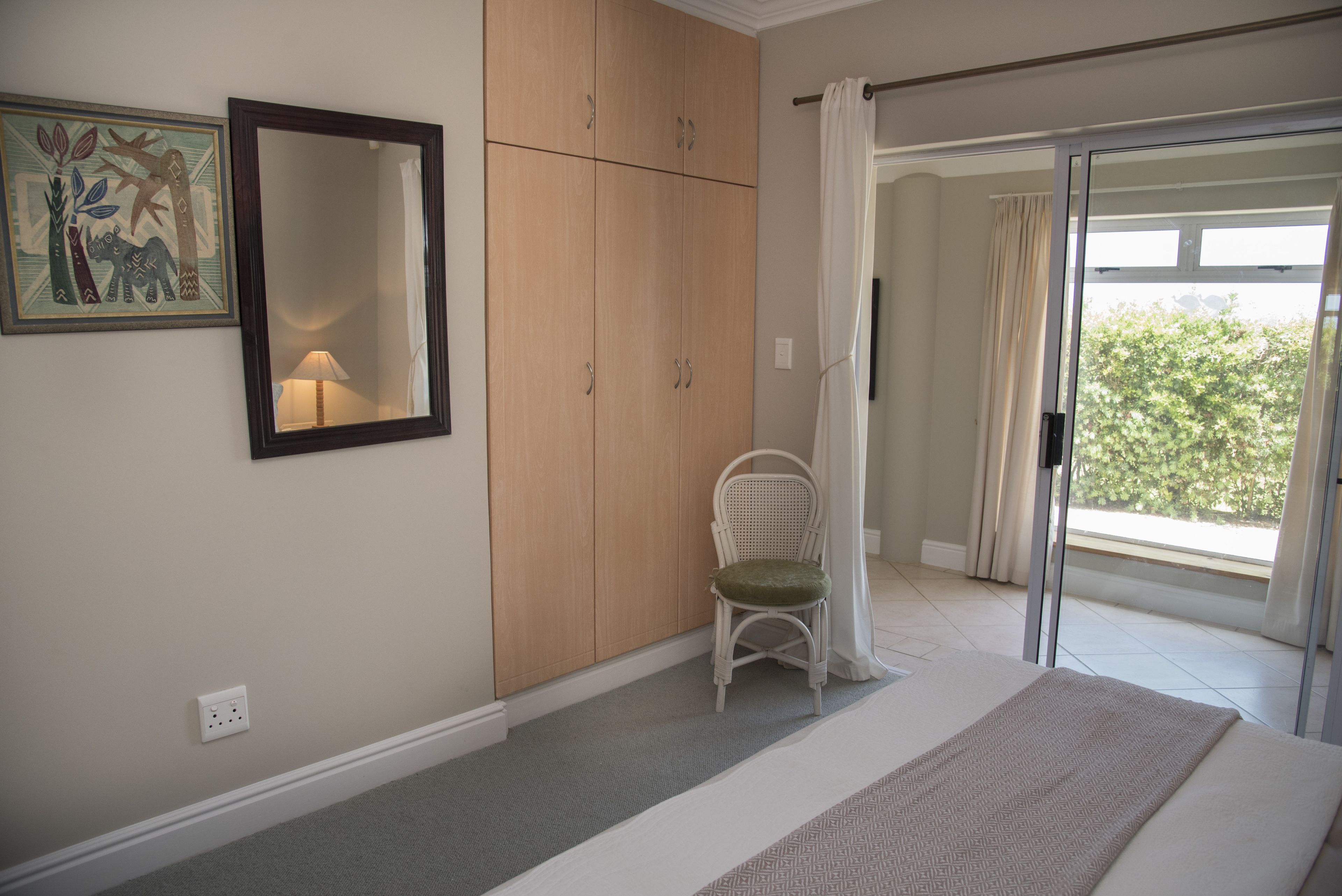 A bedroom with a bed, a chair, a wardrobe, a mirror, and a window with curtains.