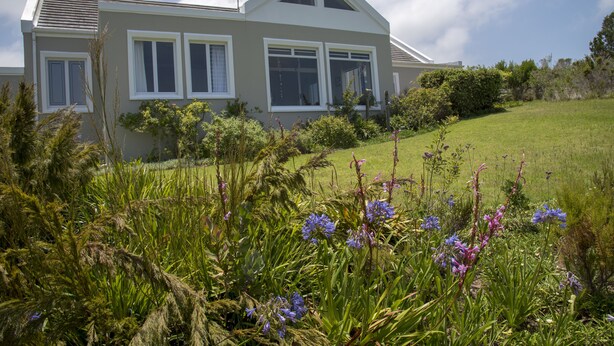 A house with a sloped roof, large windows, and a well-maintained lawn with various plants and flowers. - 20 Dunnage (Knysna)