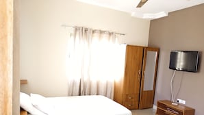 A bedroom with a wooden bed, a wardrobe, a television mounted on the wall, and a ceiling fan. - Ronna apartments at Lakeside Estates (Madina)