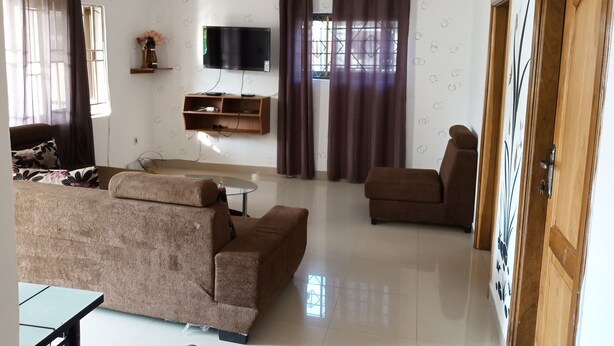 A living room with a sofa, a coffee table, a TV, and a wooden cabinet. - Ronna apartments at Lakeside Estates (Madina)