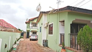 A two-story house with a satellite dish, a car parked in the driveway, and potted plants along the pathway. - Ronna apartments at Lakeside Estates (Madina)