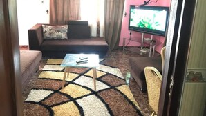 A living room with a sofa, a glass coffee table, a TV, and a patterned rug. - Ronna apartments at Lakeside Estates (Madina)