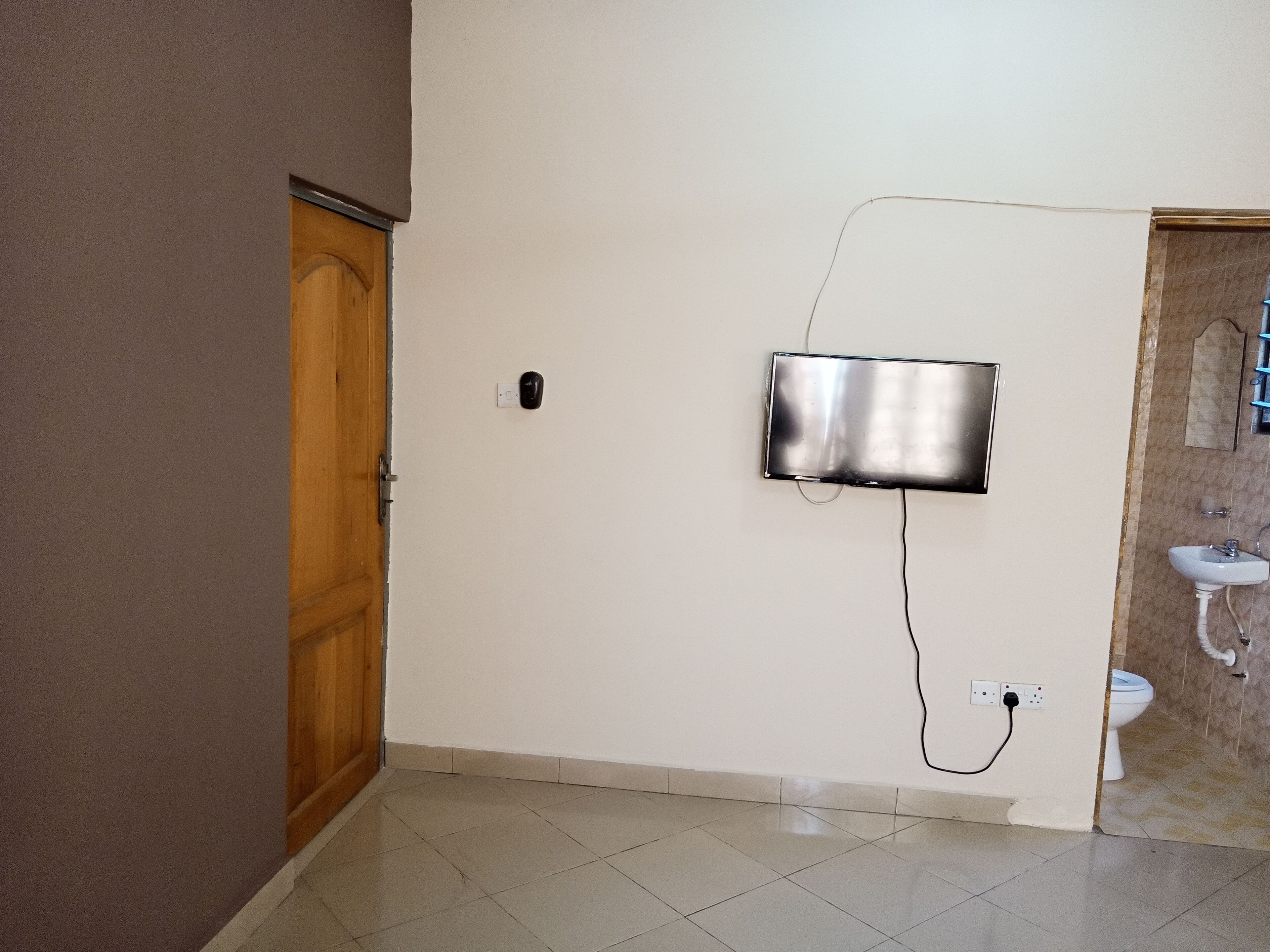 A bathroom with a toilet, sink, and a wall-mounted TV.