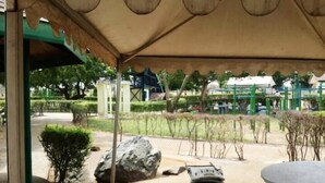 A covered outdoor area with a table and chairs, a large rock, and a stack of blue and white objects. - Ronna apartments at Lakeside Estates (Madina)
