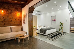 Un dormitorio moderno con techo de madera, un sofá, una cama con manta gris y una pequeña mesa con un jarrón.