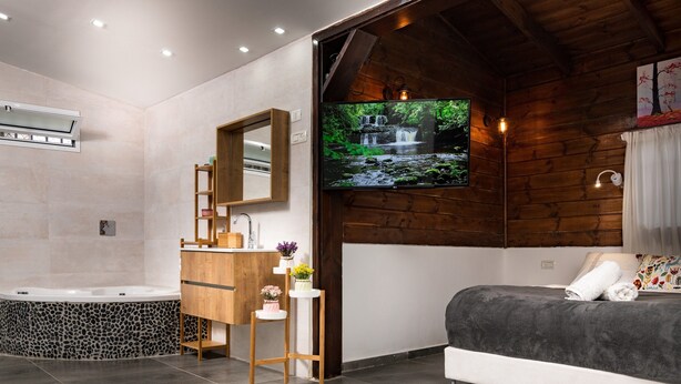 A modern bathroom with a stone-tiled bathtub, wooden vanity, and a large mirror. - Kinneret Lodging (Tiberias)