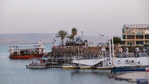 A harbor with boats docked, a rocky breakwater, and a building with a distinctive leaf design. - Kinneret Lodging (Tiberias)