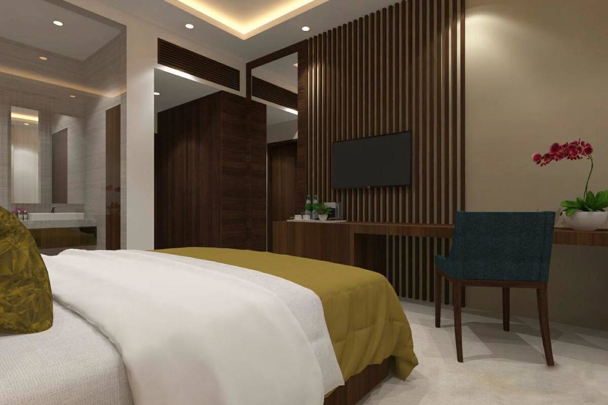 Una habitación de hotel moderna con una cama, un escritorio con silla, un televisor y una planta en maceta.