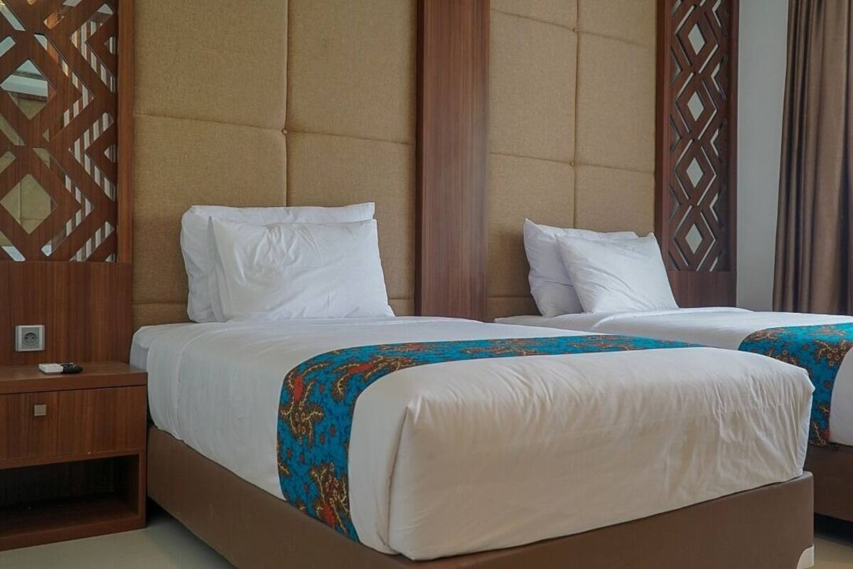 Una habitación de hotel con dos camas, una mesita de noche de madera y un panel decorativo en la pared.